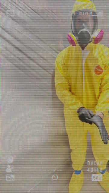 A technician wearing yellow protective clothing and a respirator